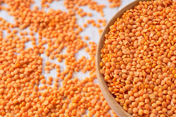 Organic red lentils are scattered out of the wooden bowl on a light table, selective focus.
