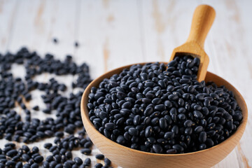 Raw black beans are scattered in a wooden bowl close up.