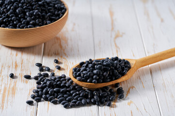 Raw black beans crumble from in a wooden spoon on a white wooden table.