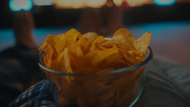 In the evening, in their home cinema, a young couple enjoys spending time together, cozying up on the sofa, snacking on chips and watching exciting episodes of their favorite TV series
