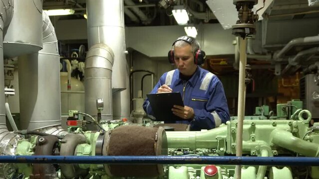 Marine Engineer in blue overall working in Engine room of ship. Work at sea. Motorman.