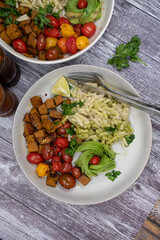 Vegan bowls- seitan cubes, vegan pesto and macaroni, roasted cherry tomatoes.  Wooden table, copy space.