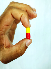 Black male hand holding a colorfull pill isolated on a white background
