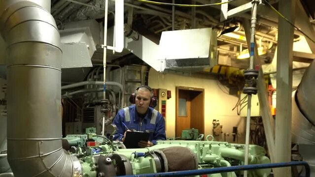 Marine Engineer in blue overall working in Engine room of ship. Work at sea. Motorman.