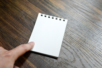 Obraz premium Hand pointing at blank white paper of notebook on wooden patterned desk background at office.