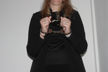A blonde woman stands with her hands handcuffed in front of her after being arrested