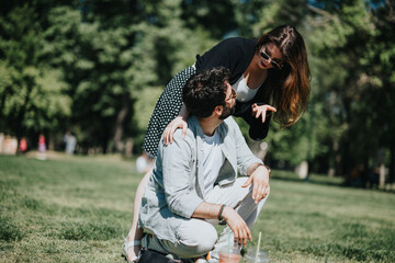 A young woman playfully leans over a seated man in a vibrant park setting, conveying a sense of joy...