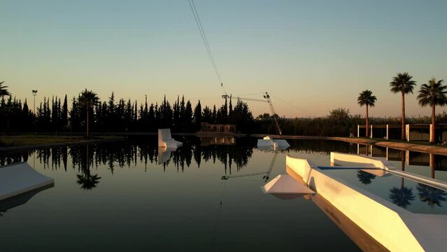 Sunrise in the wakepark. the drone rises in the water, the golden sunlight is beautifully reflected in the foreground, palm trees grow on the shore. while everyone is sleeping High quality 4k footage.