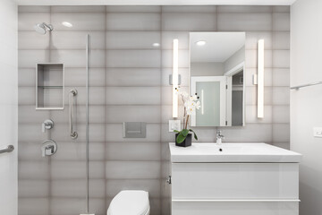 A bathroom detail with a white cabinet, grey glass rectangle tiled accent wall, and a shower with a...