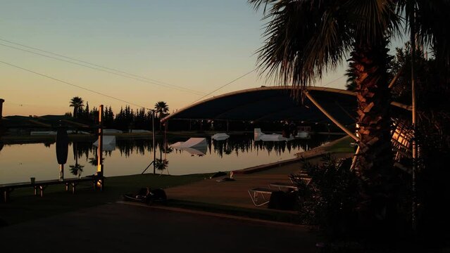 Sunrise in the wakepark. the drone rises up in the water the golden sunlight is beautifully reflected in the foreground a palm tree is growing no one has woken up yet. High quality 4k footage