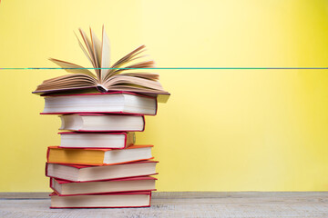 Composition with hardback books, fanned pages on wooden deck table and yellow background. Books stacking. Back to school. Copy Space. Education background.