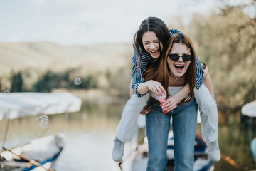 Joyful moment captured as two friends laugh together outdoors, with one riding piggyback and...