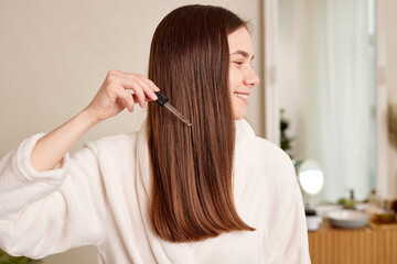 Fototapeta premium A young woman applies a drop of oil from a pipette to her hair, close-up. Vitamins, keratin for treatment, strengthening and growth of hair. Problems with dandruff, hair loss. Hair care concept