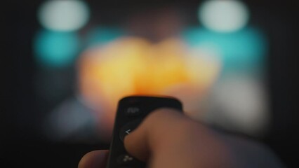 A young modern man watches TV, switching channels with a remote control. Controlling television using the TV remote control. Home cinema man relaxing in the evening sitting on the sofa