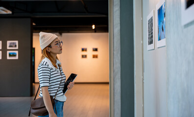 Asian woman holding tablet at art gallery collection in front framed paintings pictures on white...