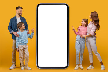 A smiling father, mother, daughter, and son stand together beside an oversized smartphone with a...