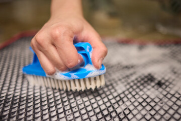 Using a brush, a person cleans a rug made of textile on the hardwood floor