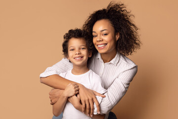 A joyful African American mother is tightly hugging her curly-haired young son, who radiates...