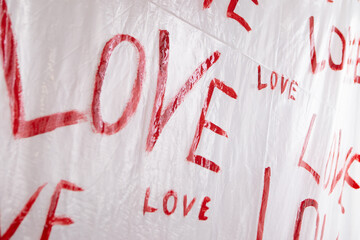 Multiple drawings of the word LOVE hand-painted in bright red forming a pattern on a plain white surface oilcloth, Valentine`s day concept celebration decoration in photo studio. Love, holiday, party
