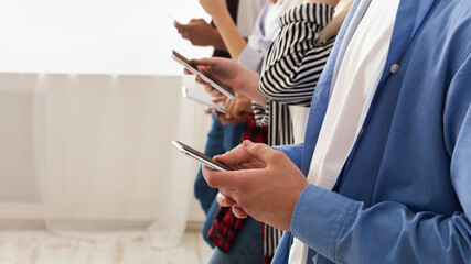Cropped of friends standing together, holding cell phones in their hands. They appear engrossed in...