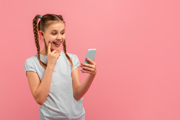 A young girl is smiling while holding a cell phone in her hand, touching her face, posing isolated...