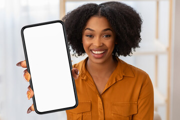 Black woman is holding a cell phone up in front of her, the screen displaying nothing but blankness, office interior