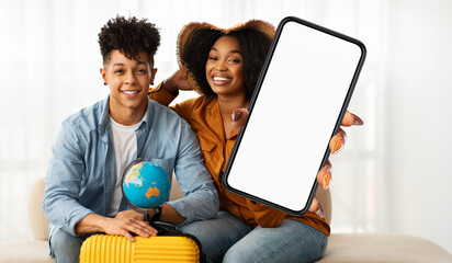 A young, smiling black couple sits closely together, holding a blank-screen smartphone suitable for...