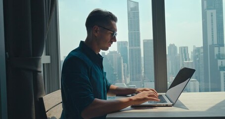 Caucasian mid adult person put on glasses opening laptop start work home office typing keyboard. Seated at desk home office millennial male working on computer success in world of home office.