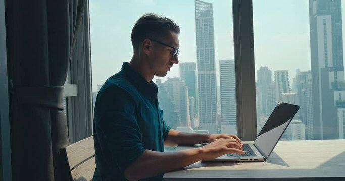 Caucasian mid adult person put on glasses opening laptop start work home office typing keyboard. Seated at desk home office millennial male working on computer success in world of home office.