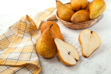 Whole and halves of pears, wicker basket and yellow kitchen towel on white wooden background..