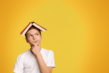 Pensive boy with book on head thinking on orange background, panorama with copy space