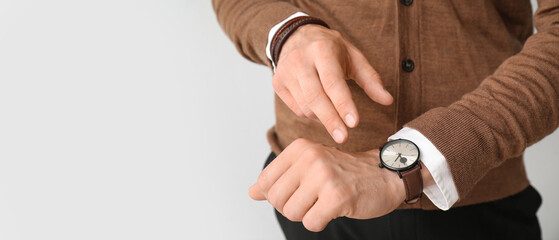 Stylish young man looking at wristwatch on grey background