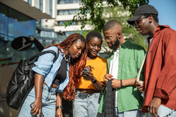 Interested stylish group of african american young people students looking at smartphone while...