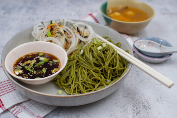 Vegan green tea noodles (matcha noodles)  and dipping sauce, daikon salad. White bowl, chopsticks, miso soup