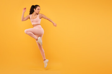 A woman wearing a pink outfit is captured mid-air as she jumps. Her joyful expression is evident as...