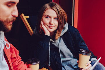 Pretty hipster girl with coffee to go in hand attentively listening boyfriend dressed in casual...