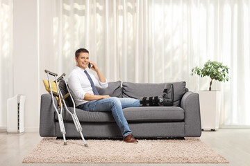 Man with a foot injury and leg brace sitting on a sofa and using a smartphone