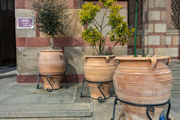 A row of clay pots with curved handles and decorative rims, placed on metal stands, showcase olive...