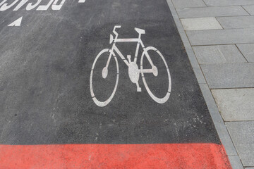 A white bicycle symbol on a black asphalt road, bordered by a red line, indicating a designated...