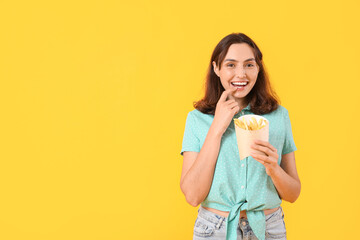 Beautiful young woman with french fries on yellow background