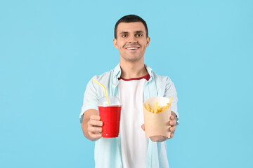 Young man with french fries and cola on blue background