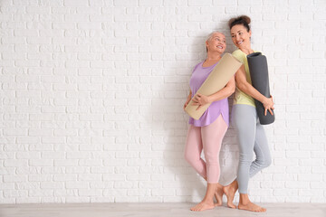 Mature women with yoga mats near white brick wall