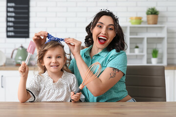 Beautiful pin-up woman and her daughter with cooking utensils in kitchen