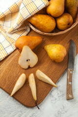 Cutting board with whole and slices pears, wicker basket and yellow kitchen towel on white wooden...