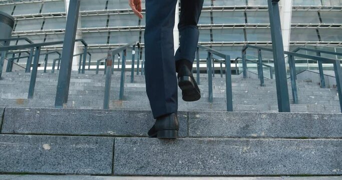 Young employee decisively climbs steps of office. Purposefully overcomes steps on path to professional success. Concrete staircase symbolizes rise of young specialist career ladder.