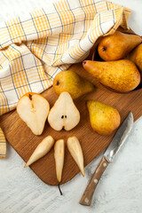 Cutting board with whole and slices pears, wicker basket and yellow kitchen towel on white wooden...