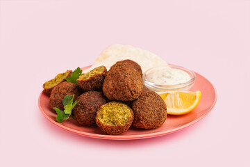 Plate with delicious falafel balls, lemon and sauce on pink background
