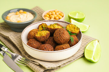 Bowl with delicious falafel balls, hummus and lime on green background, closeup