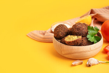 Wooden bowl with delicious falafel balls and garlic on orange background