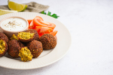Plate with delicious falafel balls, tomatoes and sauce on light background, closeup